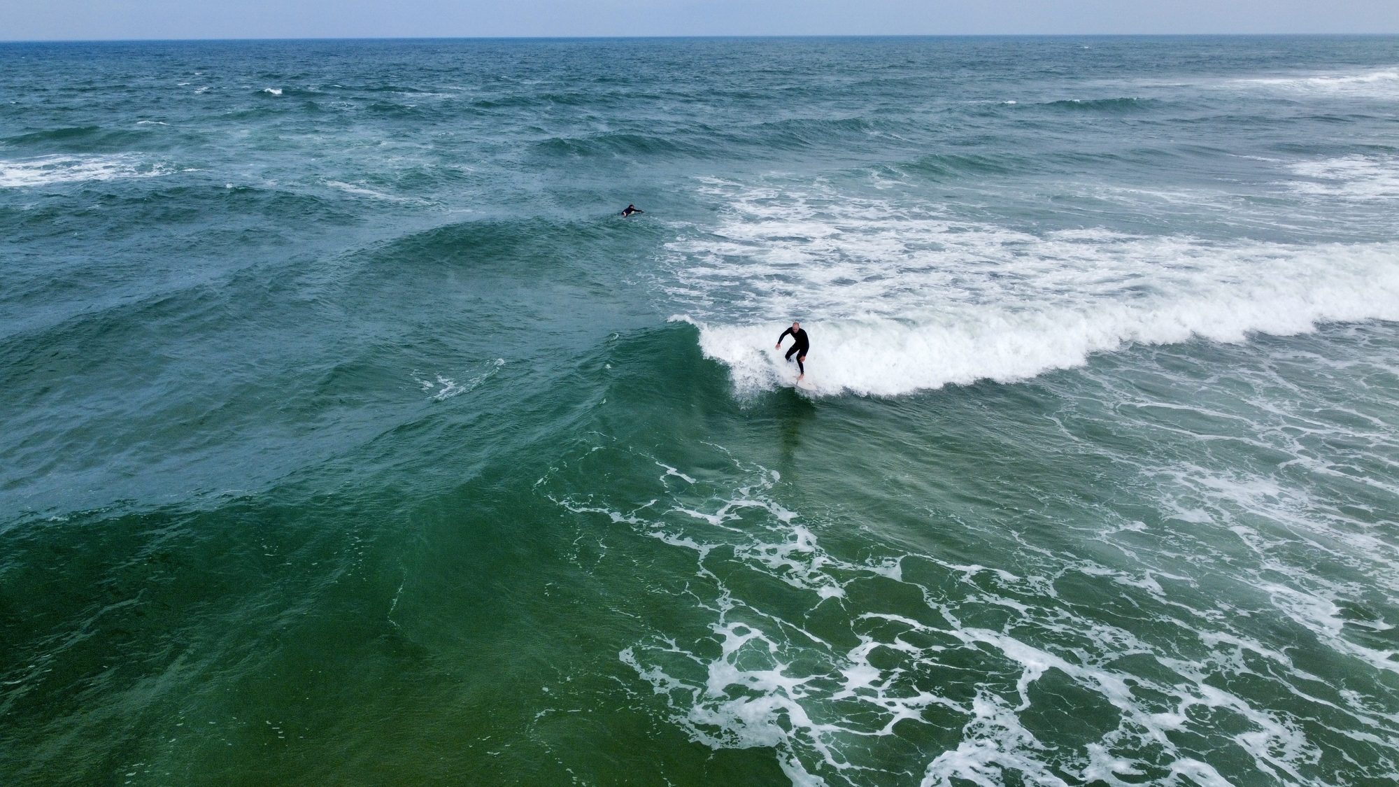 Un surfeur prend une vague au large, filmé en vue aérienne par drone